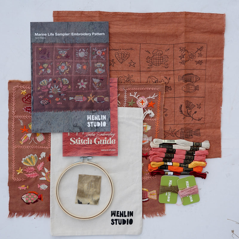 Embroidery kit contents from Menlin Studio arranged on a white background, including a pattern booklet, stitch guide, fabric samples with embroidered fish motifs, embroidery floss in multiple colors, and an embroidery hoop.